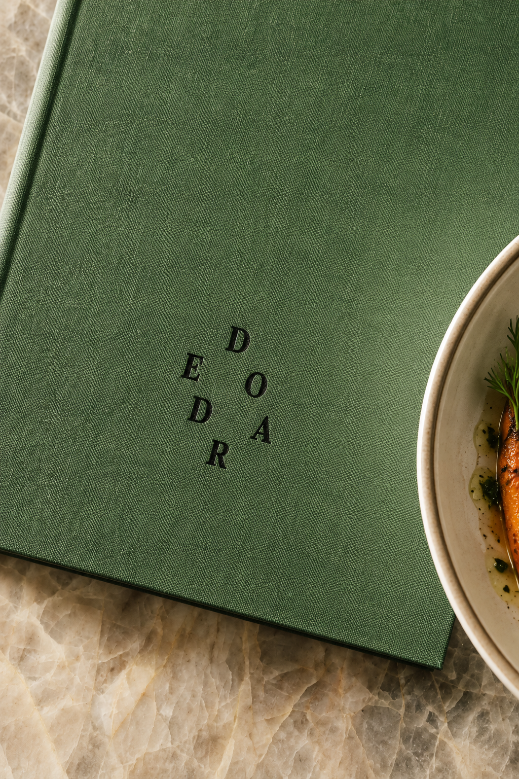 Olive linen with Deodar’s scattered letter emblem beside a ceramic plate